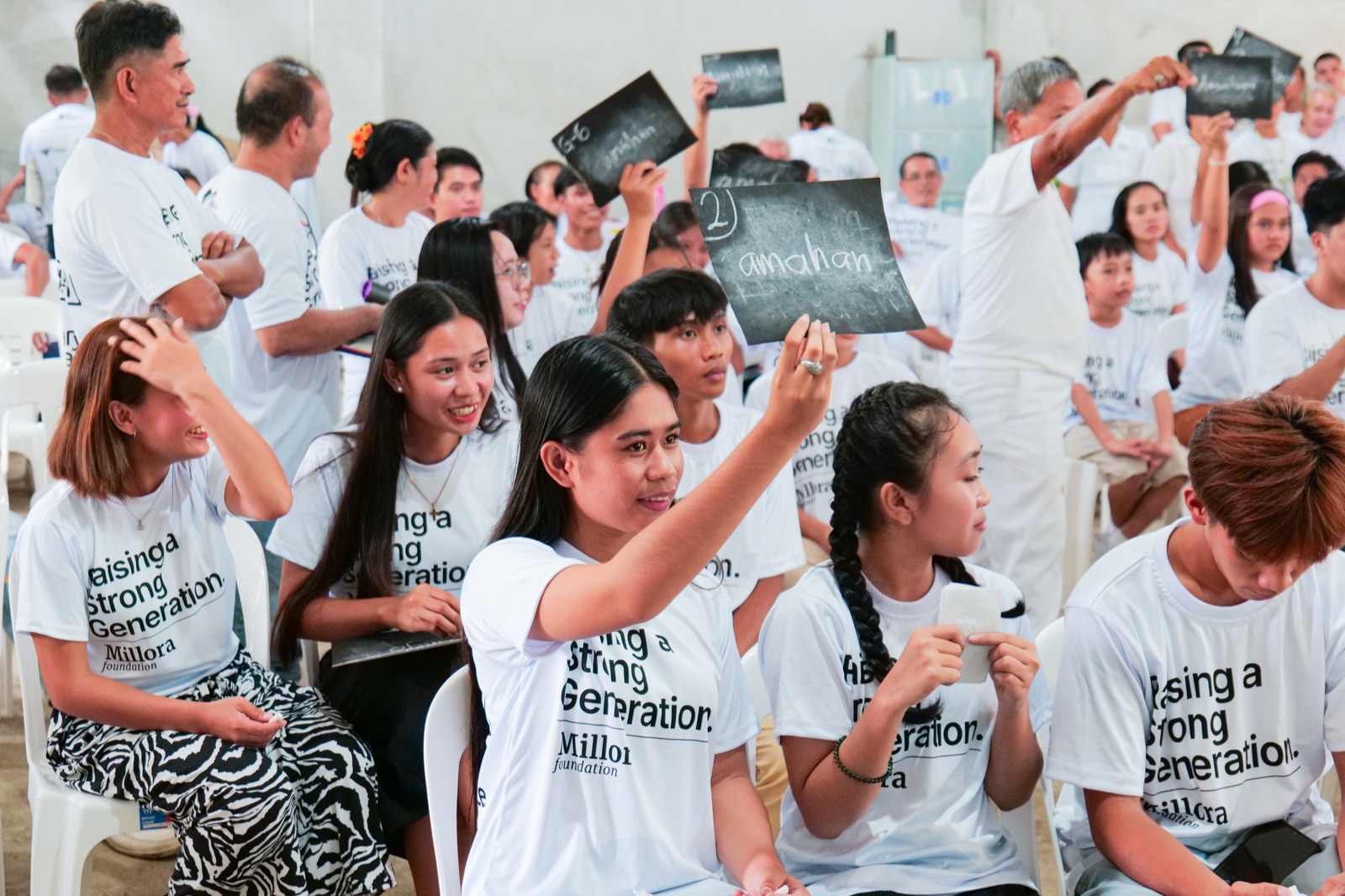 Participants in Millora Foundation shirts raise small answer boards during a group activity.