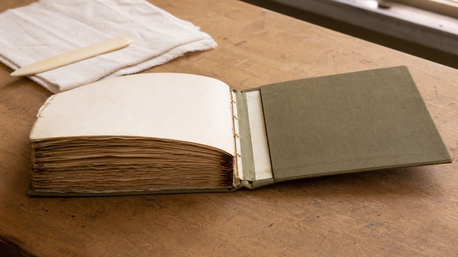 An old book block being fitted into a new muted-olive linen binding