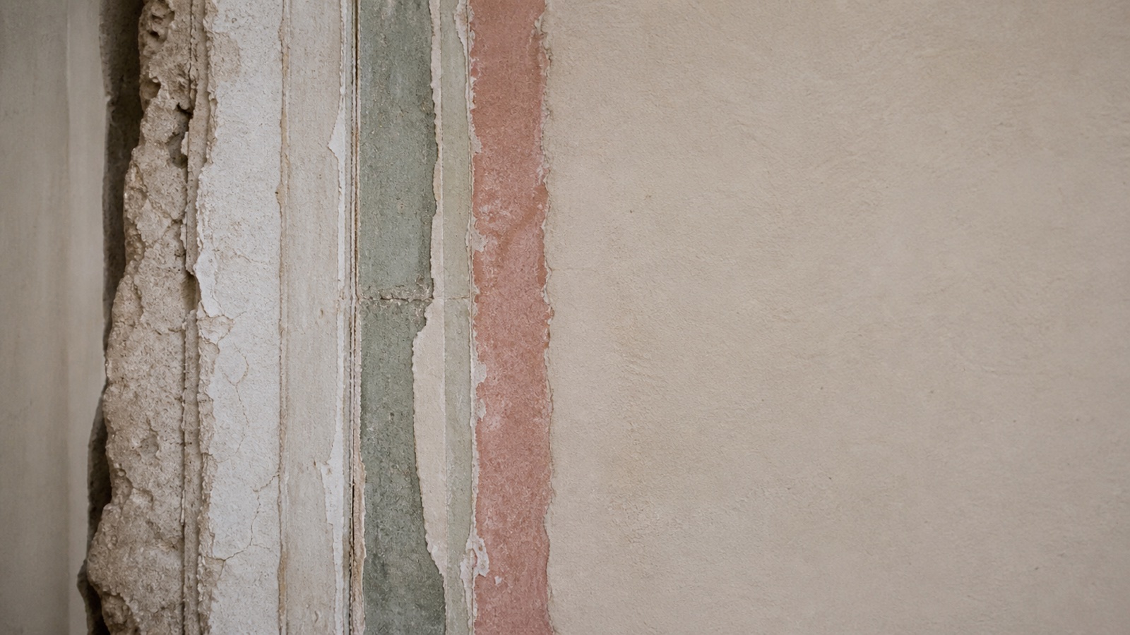 Several historical layers of paint and plaster revealed at the edge of a stable old wall