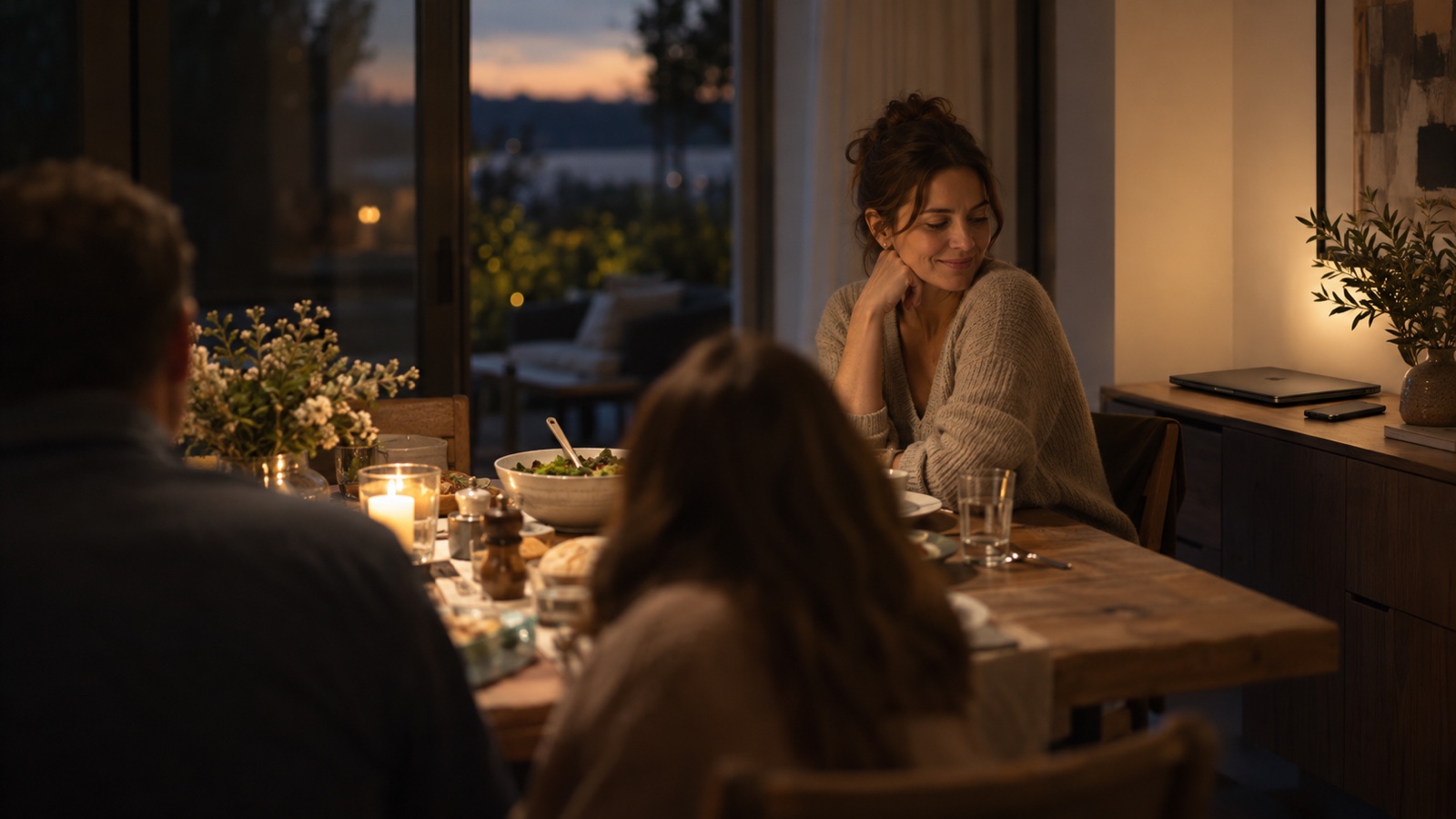 A woman founder sits with family while her closed laptop rests away from the dinner table